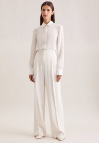 Witte button-up shirt met kraag en lange mouwen, gecombineerd met hoge taille, wijde broek in een vergelijkbare kleur. Gladde, lichte stof.