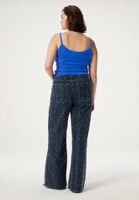 Aansluitend blauwe fuzzy tanktop gecombineerd met wijde, donkerblauwe textuurbroek, met een subtiel patroon en een verwaaid zoom.