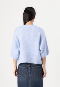 Pull tricoté bleu clair à manches courtes et coupe décontractée, associé à une jupe en denim foncé avec poches arrière.