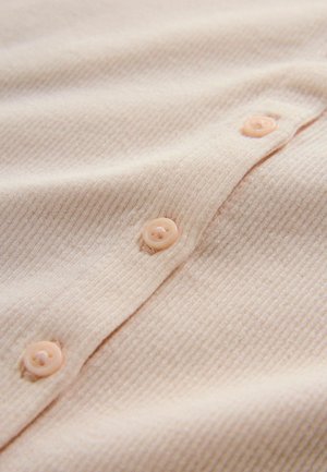 Zbliżenie na miękką beżową prążkowaną tkaninę z dopasowanymi beżowymi guzikami przyszytymi wzdłuż złożonego szwu.