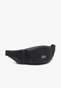 Crna fanny pack napravljena od teksturiranog materijala, s zip zatvaračem i malim kontrastnim Lacoste logom sprijeda.