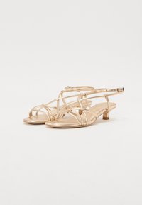 Des sandales dorées métalliques présentent un design de bride entrecroisée, un bout ouvert et un petit talon bloc, avec une bride de cheville ajustable pour un maintien optimal.