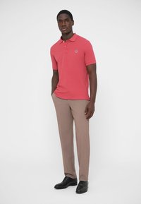 Punane polo-särk kraega, lühikeste varrukatega. Beežist lõigatud püksid, sile tekstuur. Mustad kingad, elegantne disain. Särgil peen logo.