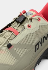 Ανοικτό καφέ παπούτσι τρεξίματος σε μονοπάτια με υφασμάτινη επάνω επιφάνεια με υφή, μαύρες και ροζ λεπτομέρειες, ενσωματωμένο κούμπωμα κορδονιών και ανθεκτική μαύρη σόλα.