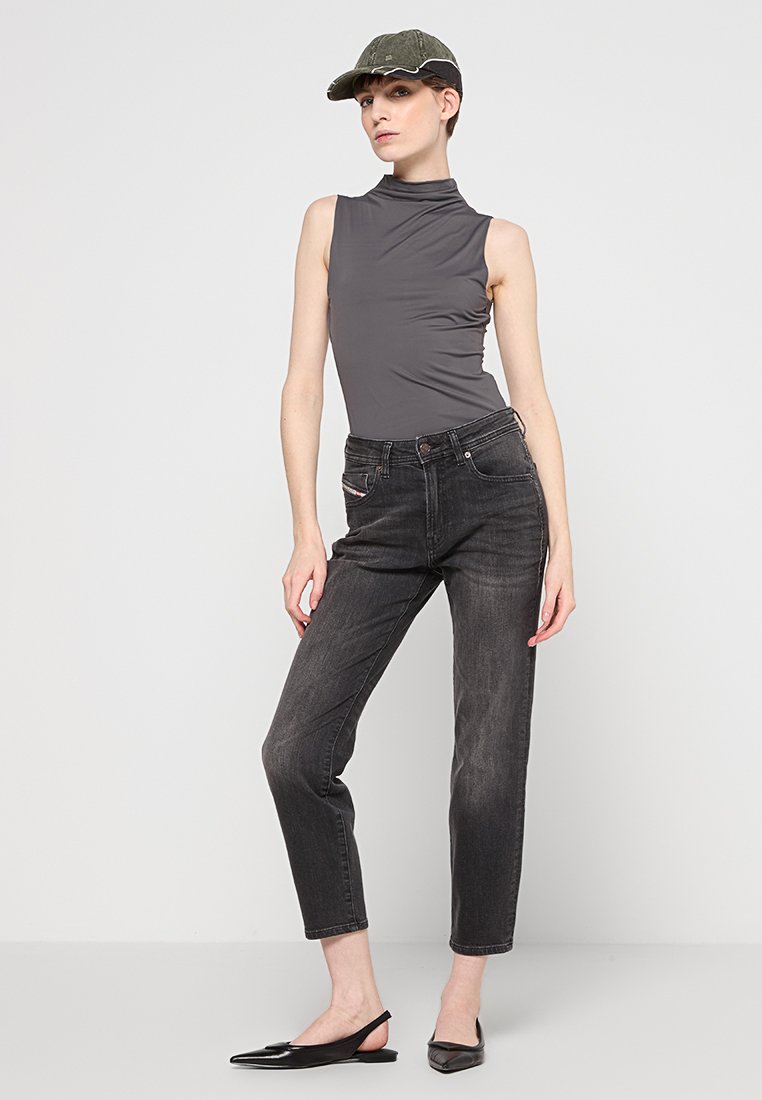 Szary bezrękawnik typu golf, czarne spodnie o wysokim stanie z delikatnym zwężeniem i czarne czółenka na spiczastym obcasie. Akcesorium: zielona czapka. Prosty fason.