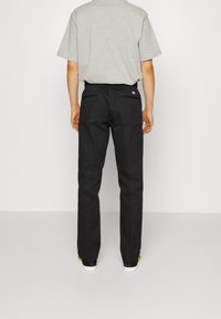 Zwarte broek met een rechte snit en een zachte textuur, voorzien van een klein logo op de achterzak, gecombineerd met een lichtgrijs T-shirt met korte mouwen.