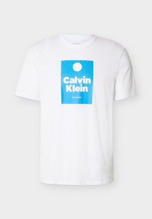 Λευκό T-shirt με κοντά μανίκια και μπλε ορθογώνιο σχέδιο, που περιέχει έναν λευκό κύκλο και το κείμενο "Calvin Klein" με έντονα λευκά γράμματα.