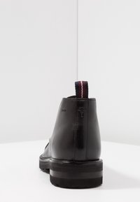 Stivale in pelle nera alla caviglia con suola chunky, linguetta posteriore con righe bordeaux e blu, e logo del marchio impressato vicino al tallone.
