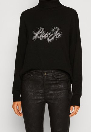 Pull col roulé noir avec texte en strass "Liu Jo" associé à un pantalon noir taille haute avec une texture subtile effet peau de serpent.
