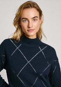 Marineblauwe trui met een geribde col en een ruitpatroon. De getextureerde stof heeft witte accenten, wat een onderscheidend ontwerp creëert.