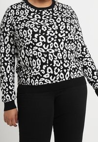 Czarny sweter z białym wzorem w cętki lamparta, z okrągłym dekoltem, długimi rękawami oraz ściągaczami przy mankietach i u dołu.