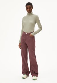 Maglione a maniche lunghe, collo alto di colore verde chiaro abbinato a pantaloni bordeaux a vita alta e gamba larga, con sneakers bianche con dettagli verdi.