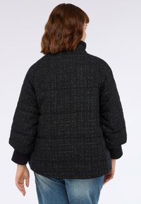 Giacca a vento nera con tessuto testurizzato e intrecciato, colletto alto e maniche oversize. Presenta un orlo inferiore aderente e polsini a contrasto.