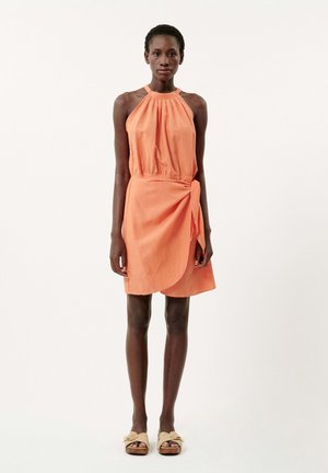 Robe à encolure halter en orange corail, présentant un corsage froncé et une jupe portefeuille asymétrique. Fabriquée en tissu léger.