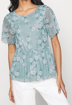 Top floreale a maniche corte in un leggero teal con design a peplo plissettato, che presenta fiori bianchi e accenti verdi su un tessuto trasparente.