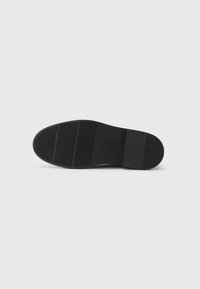 Suela de zapato negra con superficie texturizada, que presenta tres ranuras horizontales y una sección lisa en el talón. Diseño simple y funcional.