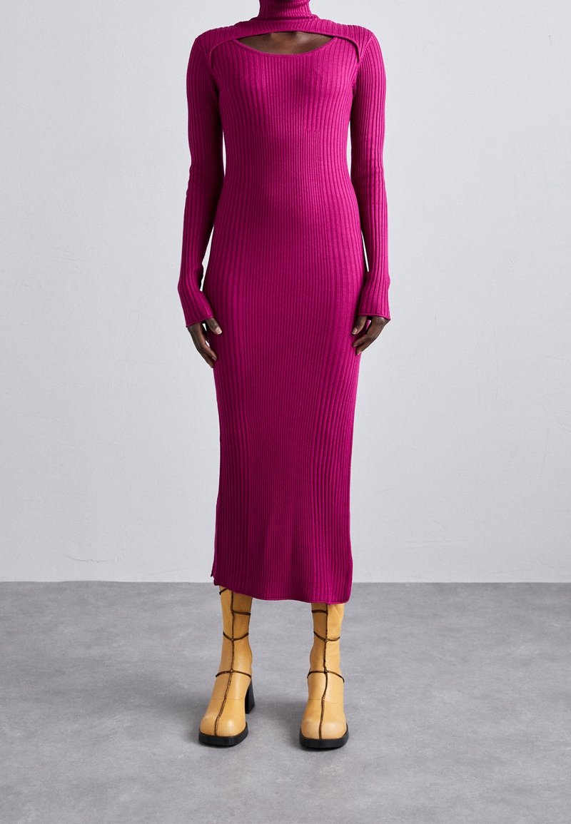 Robe longue côtelée magenta ajustée à col montant avec découpe, associée à des bottines à talons en cuir jaune avec coutures noires.