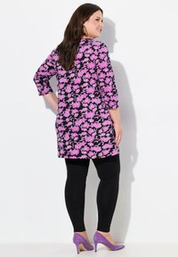 Blommig tunika i svart med rosa blommor, med trekvartsärmar. Matchas med svarta leggings och lila klackar. Slät tygstruktur.