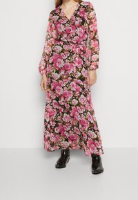 Lång, genomskinlig blommig klänning med stora rosa och vita blommor på en svart bakgrund, med V-hals, långa ärmar och knytning vid midjan.