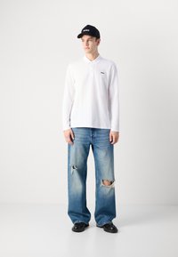 Hvit langermet polo-shirt med svart logo, kombinert med lyseblå slitte vide jeans og en svart caps med hvit skrift.