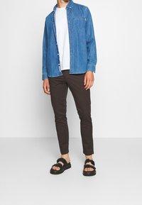 Sininen farkkupaitapusero, alla valkoinen t-paita, ruskeat kapealahkeiset housut ja mustat sandaalit, joissa on kaksi säädettävää hihnaa.