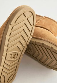 Tan suède winterboots met gestructureerde rubberen zolen, voorzien van de maatmarkering "next UK 12" op een lichte achtergrond.