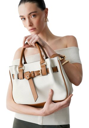 Mujer con el cabello recogido y top de hombros descubiertos sostiene un bolso de cuero blanco y marrón con detalle de hebilla.