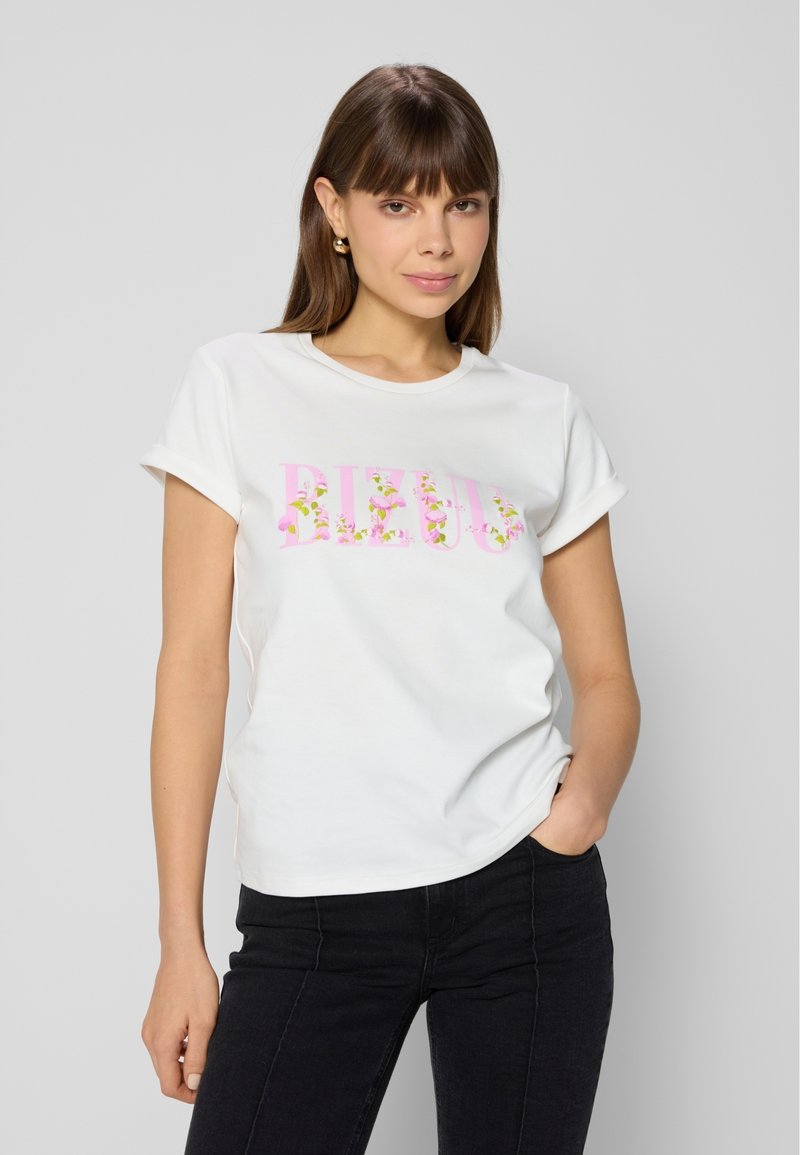Witte katoenen t-shirt met opgerolde korte mouwen en bloemenachtige roze tekst met de tekst "BEJOU." Gecombineerd met zwarte broek, wat een casual uitstraling geeft.