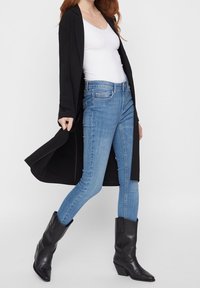 Černý dlouhý kardigan, bílý tílko, světle modré skinny džíny a černé špičaté kovbojské boty. Hladká tkanina a přiléhavý střih.