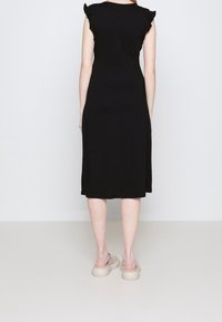 Robe noire avec manches courtes volantées, corsage ajusté et jupe fluide. Portée avec des chaussures claires à semelle épaisse.