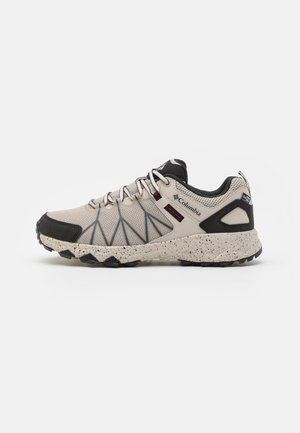 Chaussure de trail Columbia beige et noire avec tige en mesh, semelle tachetée, col rembourré et bout renforcé sur fond blanc.