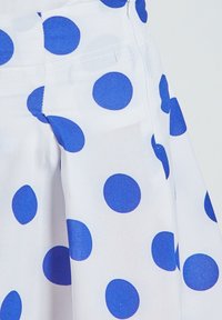 Tela blanca con grandes lunares azules, que presenta una textura suave y un diseño de falda acampanada. Incluye una cinturilla visible y bolsillo.