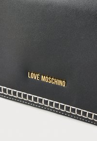 Μαύρη δερμάτινη τσάντα με υφή, με χρυσό λογότυπο "LOVE MOSCHINO" και λευκή ραφή κατά μήκος της άκρης.