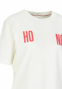 Weißes Baumwoll-T-Shirt mit kurzen Ärmeln, das auf der Vorderseite rote Blockbuchstaben "HO" und "NO" trägt sowie ein bedrucktes Etikett im inneren Nackenbereich hat.