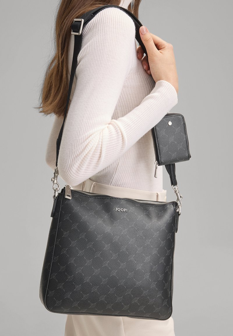 Musta, teksturoidusta nahasta valmistettu laukku, jossa on vetoketjusuljenta ja hopeanväriset metalliosat. Mukana irrotettava pienempi pussukka. Laukussa on kuvio ja logo.