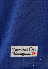 Blå mesh-stoff med små perforeringer. Har et hvitt merke med svart tekst som sier "New York City Basketball" og en rød logo.