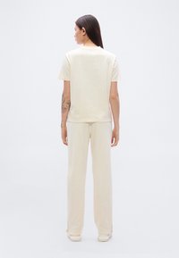 Μπεζ βαμβακερό t-shirt και παντελόνι σετ, άνετη γραμμή, απλό σχέδιο, με πλαϊνές σχισμές κοντά στο τελείωμα, λεία υφή. Πλάτη, μινιμαλιστικό στυλ.