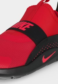 Αθλητικό παπούτσι Nike slip-on σε κόκκινο και μαύρο με υφή μπροστά, ελαστικό λουράκι πάνω με το λογότυπο της Nike και μαύρη σόλα με κόκκινες λεπτομέρειες.