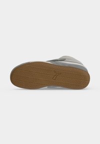 Semelle de chaussure avec une bande de roulement marron présentant un motif texturé et un petit logo Puma au centre, présenté sur un fond uni.