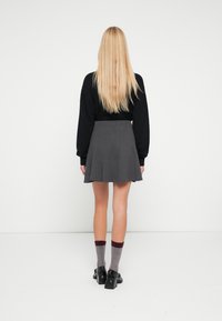 Zwarte trui, grijze geplooide rok en contrasterende grijze en kastanjebruine sokken. Model staat met lang haar, weggedraaid van de camera.