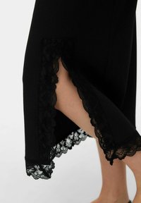 Robe noire avec texture côtelée et bordure en dentelle transparente à l'ourlet, présentant des motifs floraux mettant en valeur des fentes latérales.