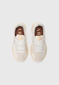 Beige und weiße Sneakers mit einem strukturierten Obermaterial aus Wildleder und Mesh, ausgestattet mit runden Schnürsenkeln und einer leicht gepolsterten Sohle. Akzentuiert mit einer braunen Innensohle.