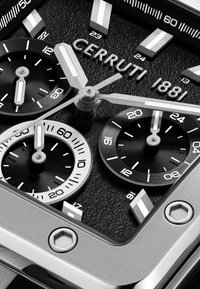 Detailní pohled na ciferník hodinek Cerruti 1881, který zobrazuje analogové ukazatele, stříbrné ručičky s luminiscenčními pruhy a texturované černé pozadí.