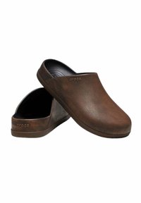 Zoccoli marroni realizzati in materiale testurizzato, con un design slip-on e punta arrotondata. Logo impresso sul lato. Fodera interna nera.