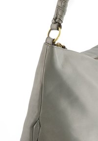 Grijze leren handtas met een gladde textuur, ronde vorm en gevlochten hengsel met messing hardware accenten. Ritsopening aan de bovenkant.