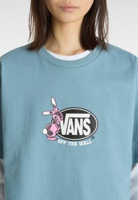 Lys blå bomulds T-shirt med korte ærmer. Har et pink tegneserie-kanin grafik ved siden af en sort og hvid "VANS OFF THE WALL" logo.