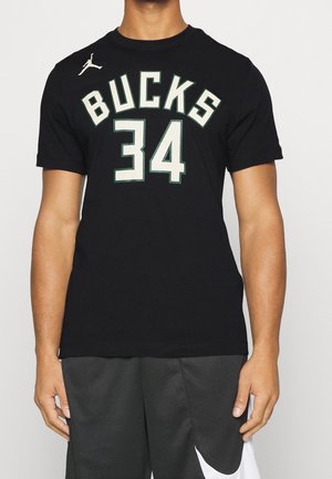 Persona vistiendo una camiseta de baloncesto negra de los Milwaukee Bucks con el número 34 y pantalones cortos negros de Nike con el logo de la marca en blanco.