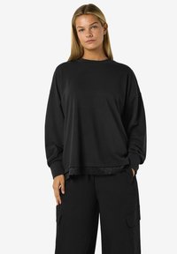 Felpa nera con una vestibilità comoda, maniche lunghe e bordo in pizzo sul fondo, abbinata a pantaloni cargo neri coordinati.