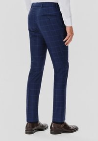 Granatowe spodnie w kratę o dopasowanym kroju, z zapiętą kieszenią z tyłu i teksturowanym materiałem. W połączeniu z brązowymi butami eleganckimi.