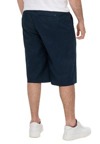 Shorts bleu marine en tissu doux, longueur genoux, avec une coupe décontractée et des poches arrière. Portés avec des baskets blanches.